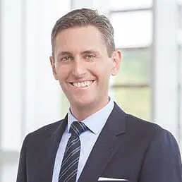 A man in a suit and tie smiling in front of a window for his headshot.