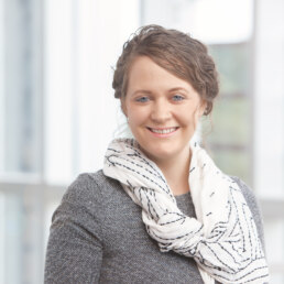 A woman smiling in front of a window for her company headshot.