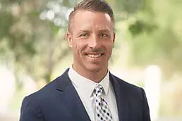 A man in a suit smiles for the camera for his company headshot.