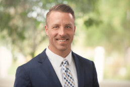 A man in a suit smiles for the camera for his company headshot.