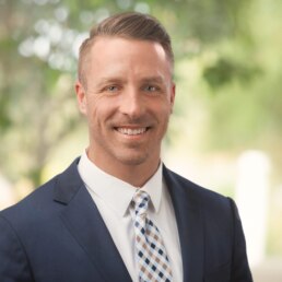 A man in a suit smiles for the camera for his company headshot.