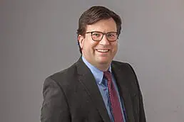 A man in a suit and tie smiling for the camera in his company headshot.