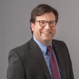 A man in a suit and tie smiling for the camera in his company headshot.