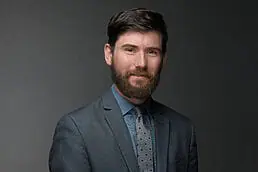 A bearded man in a suit and tie poses for a company headshot.