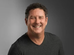 A smiling man in a black v-neck shirt for his company headshot.