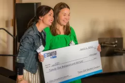 A couple of women holding a large check for an event photography project.