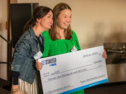 A couple of women holding a large check for an event photography project.