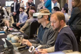 Two men are using virtual reality headsets at a company conference.