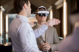 A man wearing a virtual reality headset is talking to another man at a company conference.