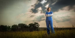 A healthcare worker in a field under a cloudy sky.