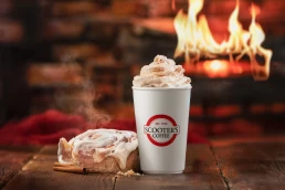 A cup of coffee with a cinnamon roll next to a fireplace, captured in exquisite detail for food photography.