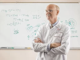 A man in a lab coat standing in front of a whiteboard for healthcare presentations.