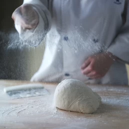 A chef sprinkling flour on a dough ball for a company headshot.