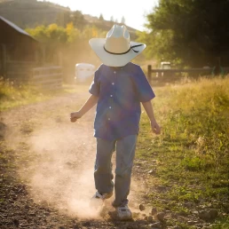 A boy wearing a cowboy hat walking down a dirt road photography shoot.