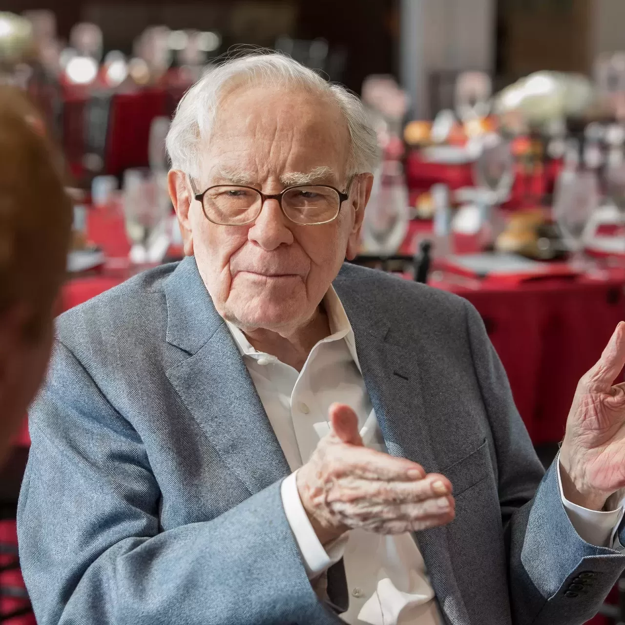 Warren Buffett speaks at a formal luncheon with attentive guests and elegant table settings.