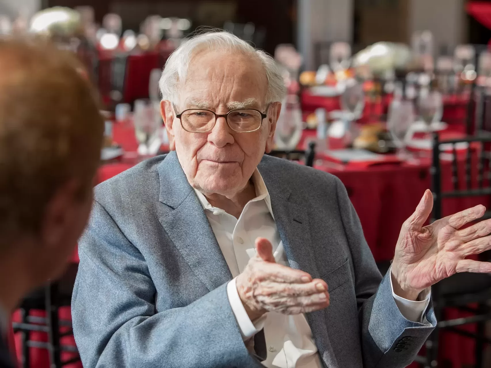 Warren Buffett speaks at a formal luncheon with attentive guests and elegant table settings.