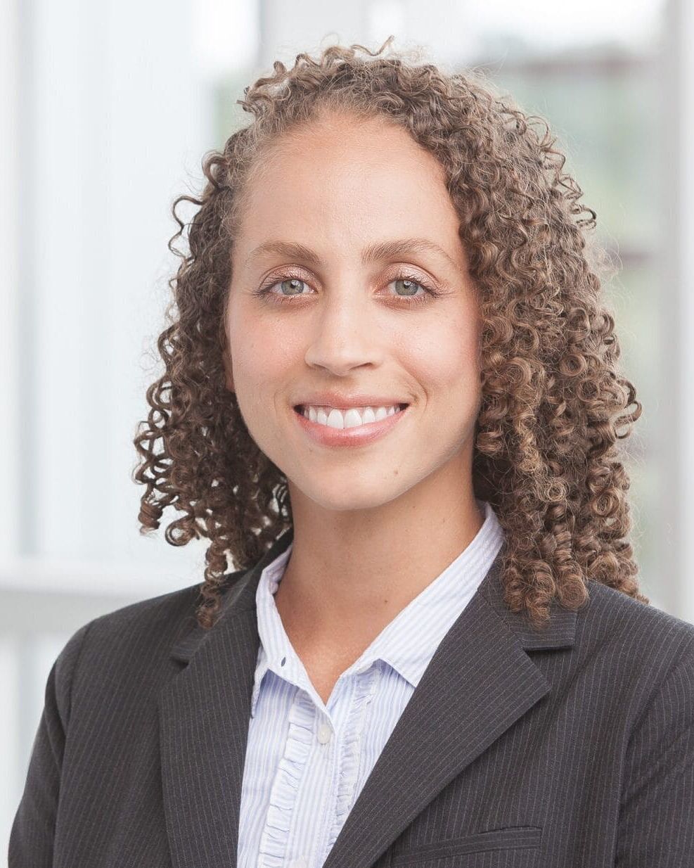 A woman with curly hair wearing a suit in her headshot.