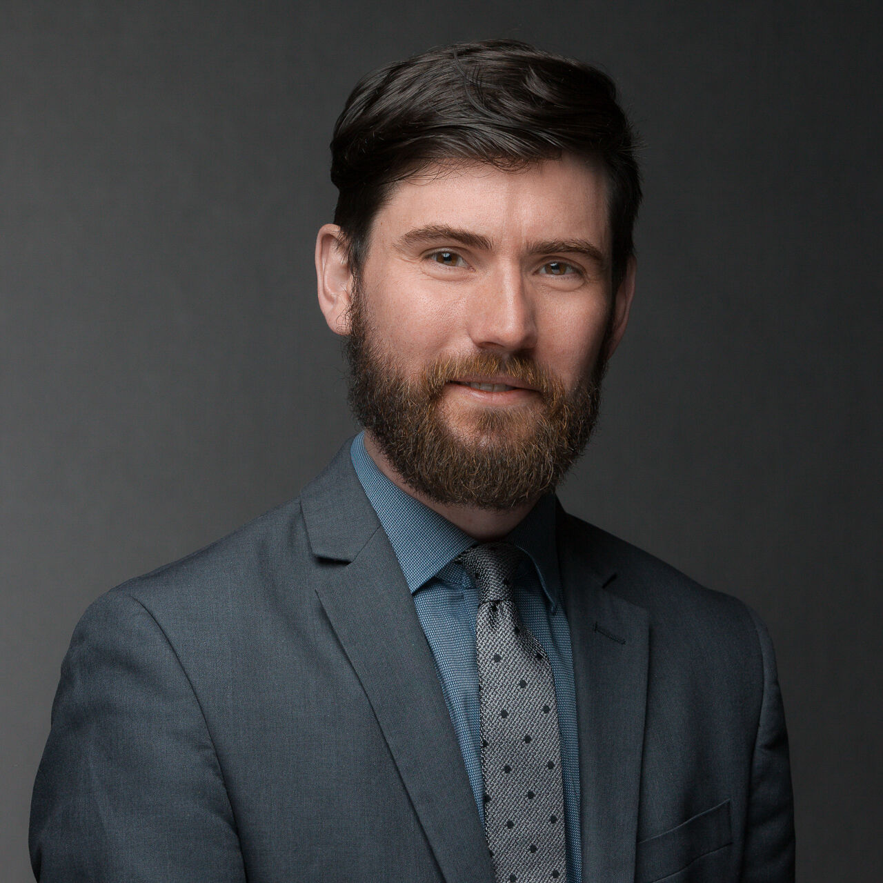 A bearded man in a suit and tie poses for a company headshot.