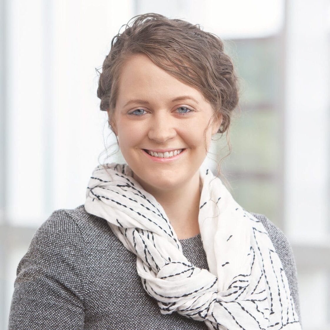 A woman smiling in front of a window for her company headshot.