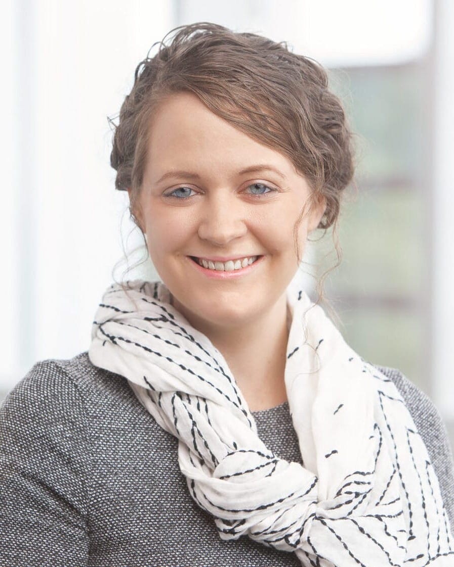 A woman smiling in front of a window for her company headshot.
