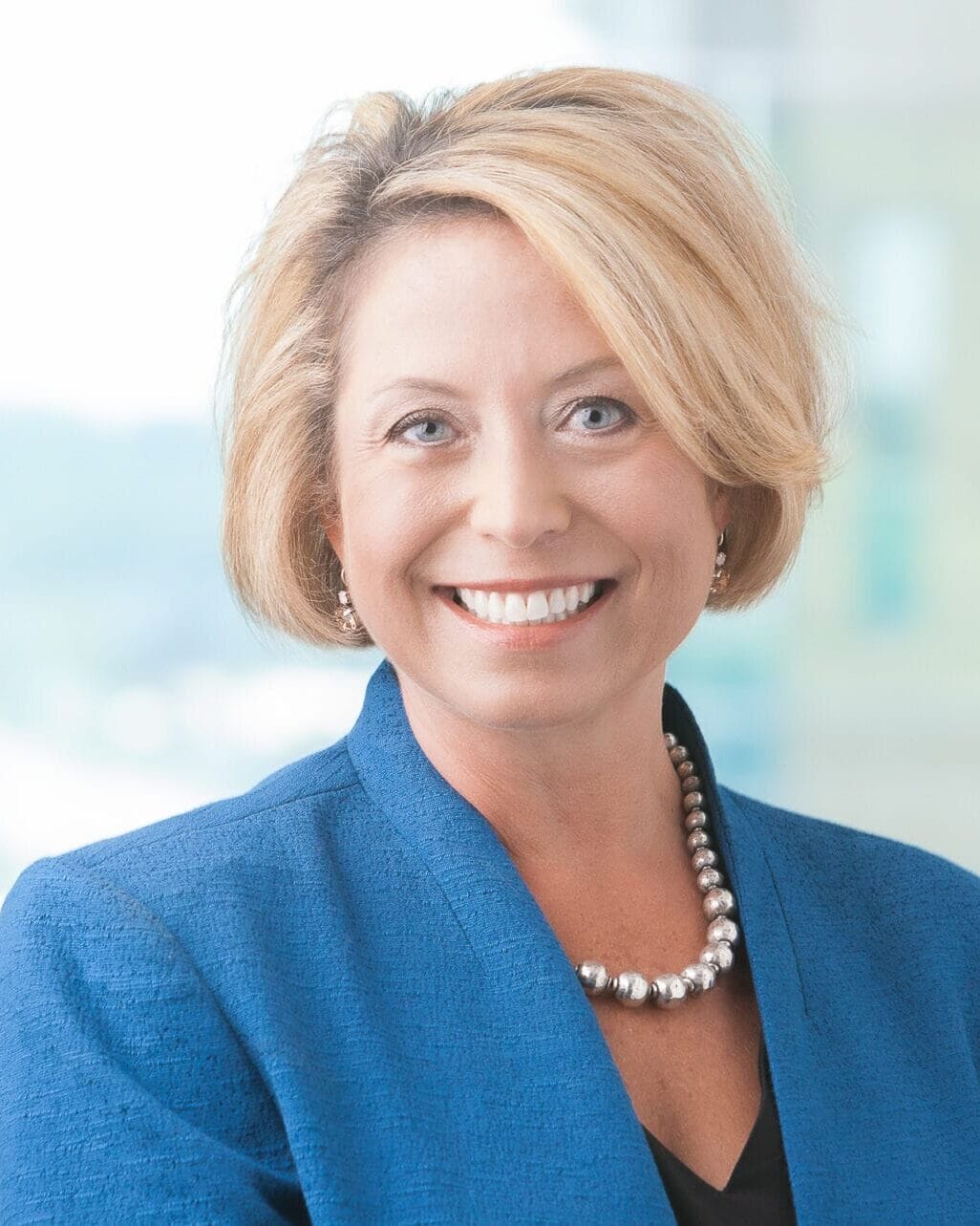A smiling woman in a blue suit poses for her company headshot.