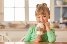 A little girl holding an ice cream cone in front of a kitchen table for Food Photography.