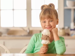 A little girl holding an ice cream cone in front of a kitchen table for Food Photography.