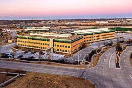 Aerial view of a modern tan brick office building with parking lot and landscaped grounds at sunrise.