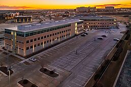 Aerial view of a modern office park at dusk with an empty parking lot and glowing sunset sky.